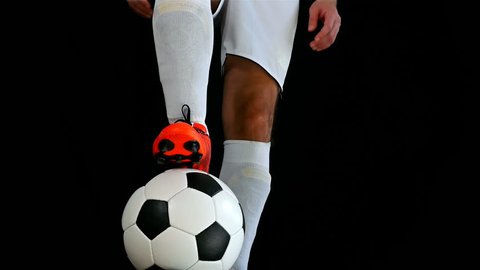 Footballer in boots putting his leg on a ball, black background