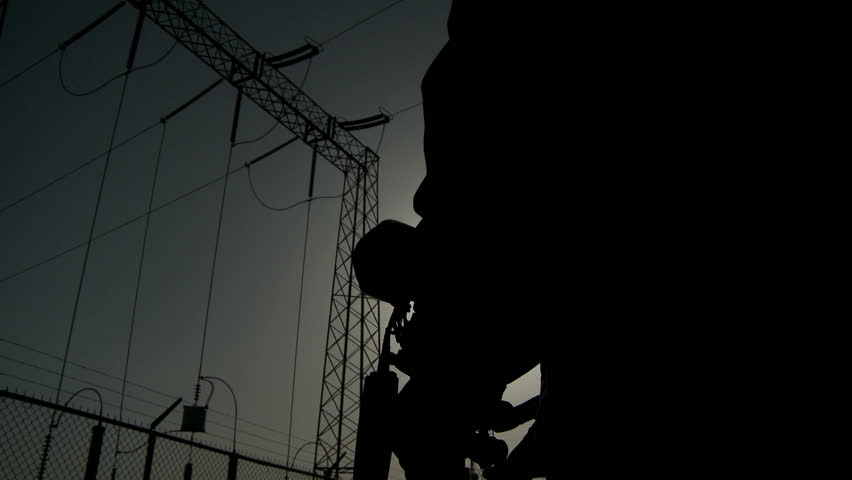 A silhouette of a person is working on a camera with a power pylon in the