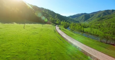Aerial UHD 4K view. Low air flight over mountain rural dirt road and meadow at sunny summer morning.