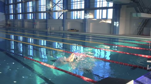 Male swimmer jumps off starting block and swims in pool video. Training start. Professional athlete on dives to water