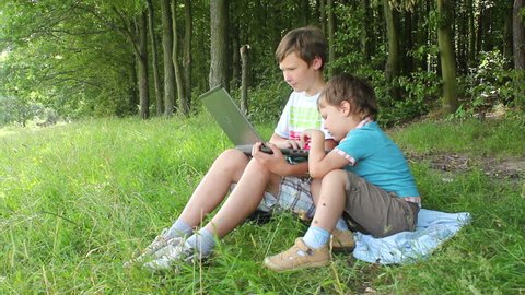 Two boys walking in the forest with a laptop