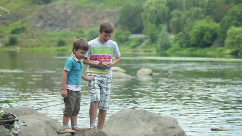 Two boys walk by the river in summer