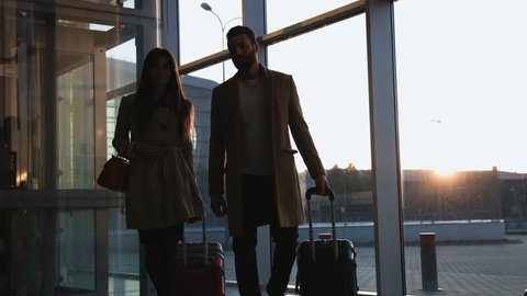 Beautiful young couple goes to the frame of the luggage at the airport sunset