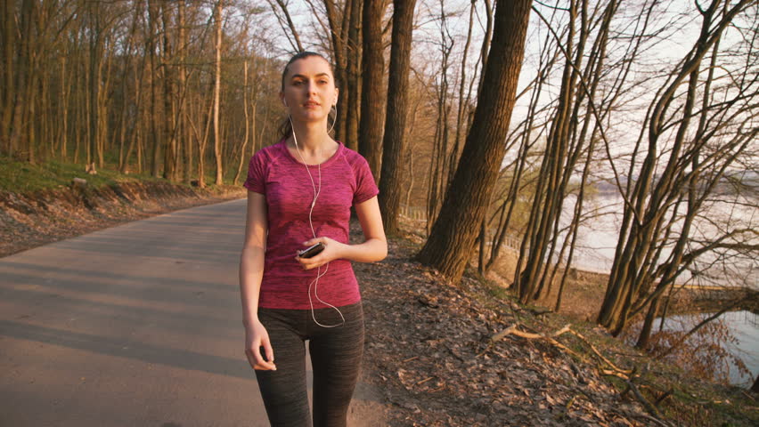 Pretty girl walking in the park and listening to the music in earphones 4K