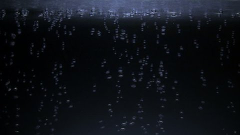 Air bubbles floating up and collecting on a liquid surface with blue light