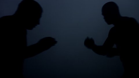 Silhouettes kick boxers fight in dark. Closeup of mma fighter silhouettes. Boxing fight in dark. Two kickboxers training at dark ring. Sparring partners fight training. Fights of mixed martial arts