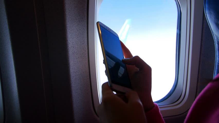 View from the airplane window, you can see the dark silhouette of female hands working on a gadget, smartphone, mobile phone, finger movement. Visible sky, clouds, weather clear, sunny day | Shutterstock HD Video #26157518