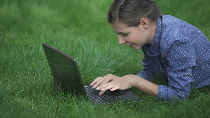Attractive business woman typing letter on the laptop and lying on the green