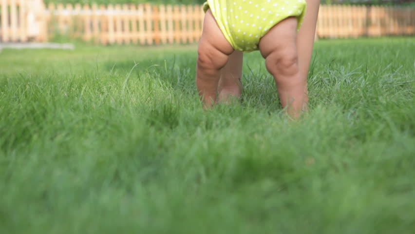Down view on legs of mother and baby walking together on green grass