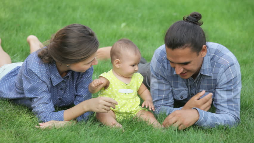 Happy parents with baby lying on the green grass