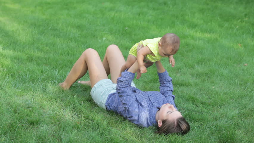 Young mother lying on the grass and playing with her toddler