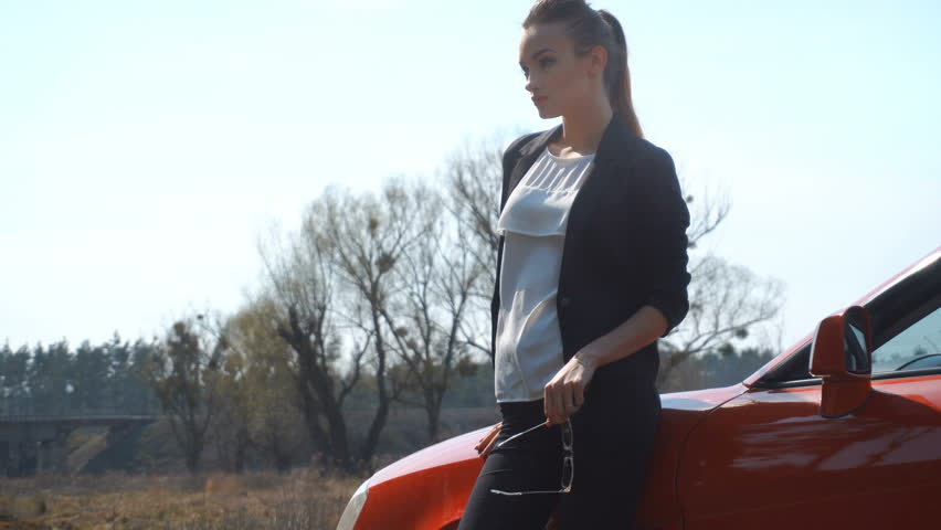 charming young girl on the red car posing on the street countryside