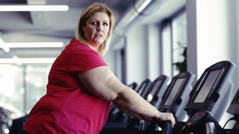 Overweight woman walking on treadmill in modern gym.