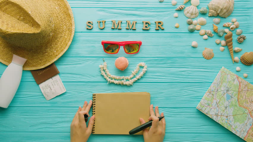 Woman hands wriiting on here notebook about summer list. Trip love. Top view. Turquoise background. Close up.