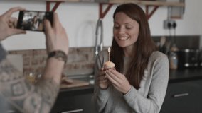 Boyfriend taking photo of girlfriend holding cupcake with candle