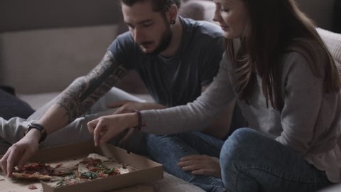 Young couple eating takeout pizza at home