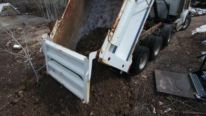 Dirt falls out of the dump truck as the vehicle moves forward and the last of the load is emptied.