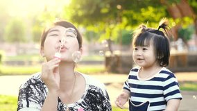 Asian Mother entertaining her baby girl by making iridescent soap bubbles