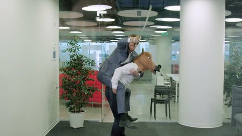 Funny scene with a positive office worker with a horse's head mask carries on his back a colleague with a katana