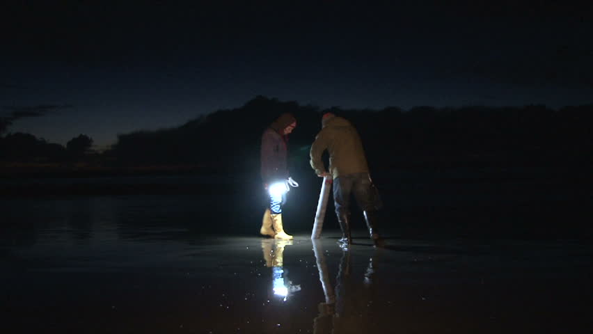 Model released man and woman couple with clamming gun catch a razor clam right before tide comes in getting woman all wet.