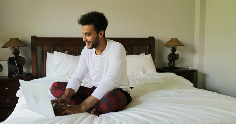 Pondering Man Using Laptop Computer Sitting On Bed Hispanic Guy Type Chatting Online In Bedroom Morning Slow Motion 60