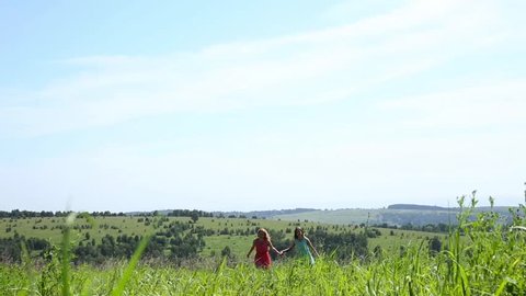 Two young girls are running on a field hand in hand, freedom and relationship concepte