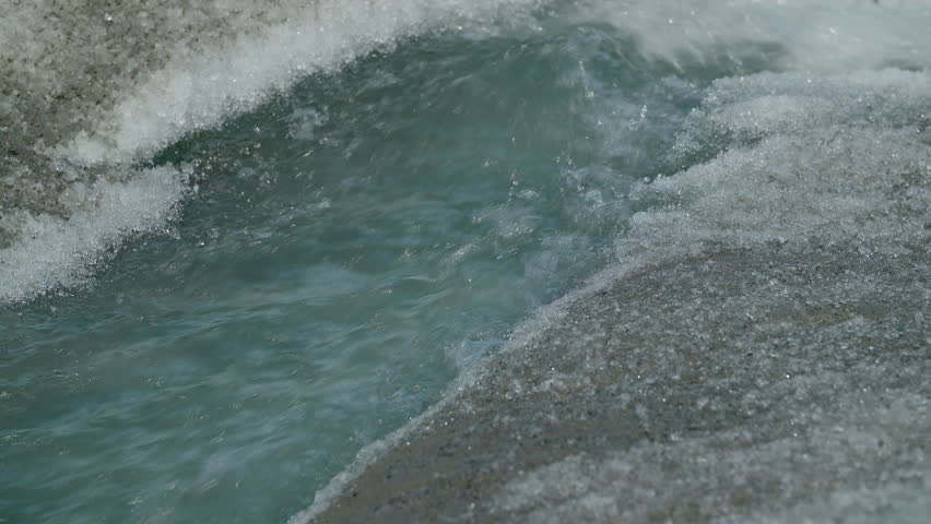 Ice river flows from melting glacier. Camera tilts up as the water flows away. 