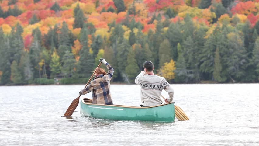 Happy couple canoeing in a lake in Canada. There are many trees on background with colourful leaves during autumn. Young and happy, enjoying a canoe trip together. Wanderlust and nature concepts
