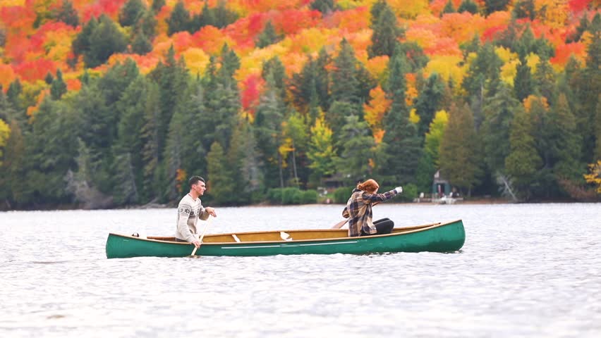 Happy couple canoeing in a lake in Canada. There are many trees on background with colourful leaves during autumn. Young and happy, enjoying a canoe trip together. Wanderlust and nature concepts