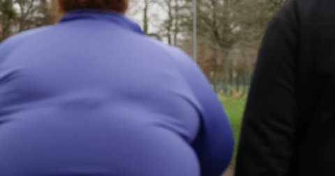4K Unhealthy overweight couple taking a walk outdoors with child in a stroller. Slow motion.