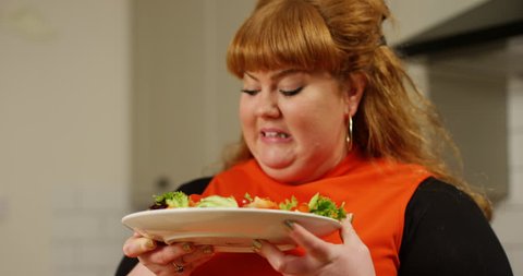 4K Overweight woman on a diet looking unimpressed at a plate of salad. Slow motion.