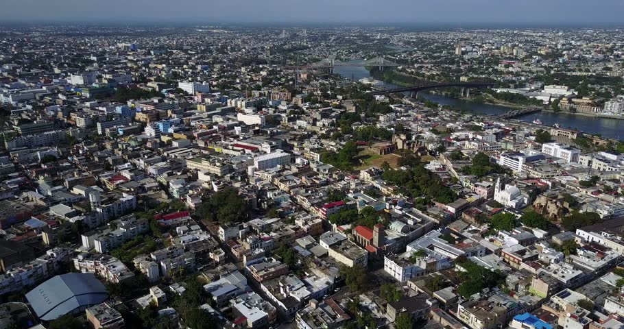 High aerial panorama above a bright Dominican Republic city with dense neighborhoods, waterways, and the Caribbean coast beyond, 2017.