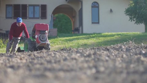 Slow motion shot of mature farmer plowing a field in the garden of his house.