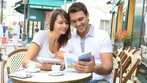 Couple on a coffee shop terrace reading tourist book
