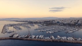 Dawn in the Greek marina, Athens. Aero video shooting. A lot of different yachts, catamarans moored to piers. In the background is the landscape of the mountains and the city houses. Summer clear