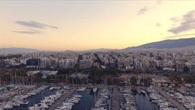 Dawn in the Greek marina, Athens. Aero video shooting. A lot of different yachts, catamarans moored to piers. In the background is the landscape of the mountains and the city houses. Summer clear