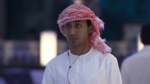 DUBAI, UAE - CIRCA FEBRUARY 2016: A busy modern mall in Arabia despite the effects of the low oil price on the economy, showing a young Arab man wearing traditional Arab dress using his smart phone.