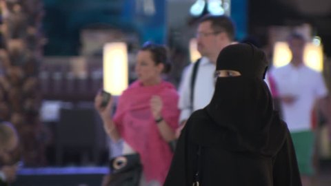 DUBAI, UAE - CIRCA FEBRUARY 2016: A busy modern mall in Arabia despite the effects of the low oil price on the economy, tracking a Saudi Arabian woman wearing a head scarf with her face fully covered.