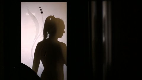 Silhouette of a woman changing clothes behind a glass door. She takes off her underwear