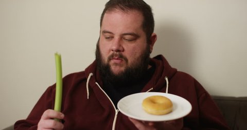 4K Overweight man on a diet making the choice to eat a celery stick or a donut