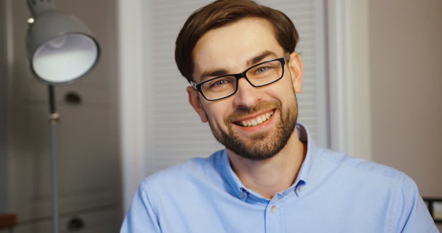 Young man possing to the camera on office background. Attractive businessman smiling on camera. Close up.