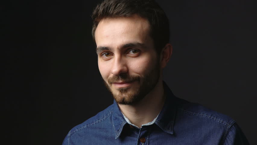 Closeup portrait of young business man looking confident smiling at camera, locked down video over dark background