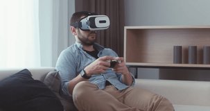 Caucasian male in casual clothes using his VR headset indoors, playing a virtual reality game at home. 4K UHD RAW edited footage 