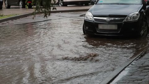 Flooding water on a pavement after heavy rain with sound. Car is near, people walk by.
