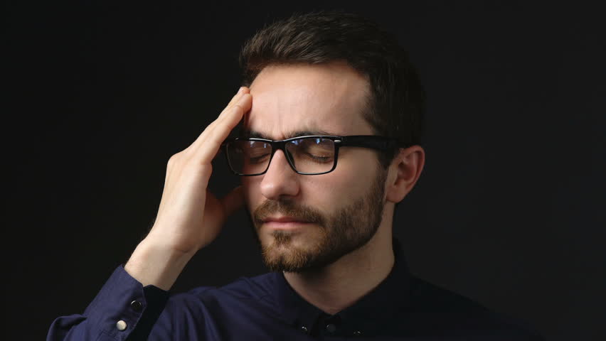 Headache, Tired, Stressed concept. Closeup portrait of young business wearing eyeglasses suffering from headache, locked down video over dark background