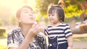 Slow motion Asian Mother entertaining her baby girl by making iridescent soap bubbles