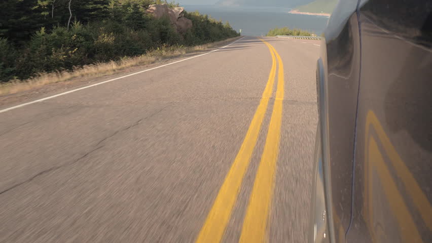 CLOSE UP: Driving on steep coastal road descending from the mountain ridge towards the North Atlantic Ocean on sunny day. People on road trip traveling on switchback highway across the Canadian coast Royalty-Free Stock Footage #26241194