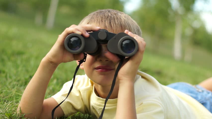 Closeup portrait of a boy looking through binoculars at camera
