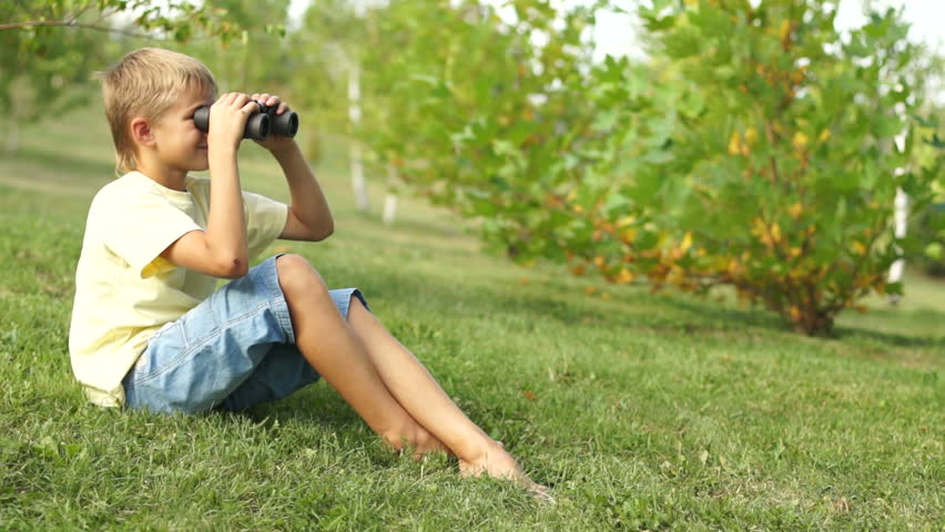 Boy watching with binoculars sitting on the grass
