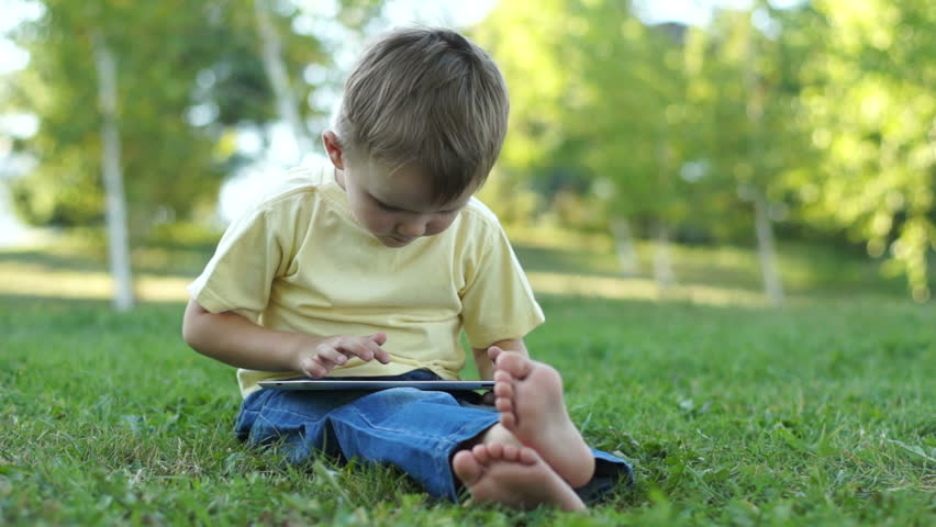 Little boy using a tablet pc outdoors and sitting on the grass
